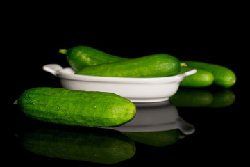 Group of five whole fresh green baby cucumber in white oval ceramic bowl isolated on black glass