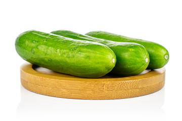 Group of three whole fresh green baby cucumber on bamboo coaster isolated on white background