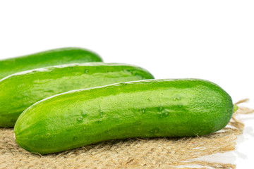 Group of three whole fresh green baby cucumber on natural sackcloth isolated on white background