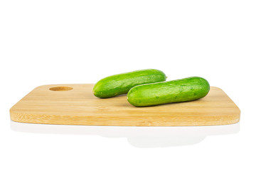 Group of two whole fresh green baby cucumber on bamboo cutting board isolated on white background