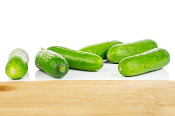 Group of six whole fresh green baby cucumber on bamboo cutting board isolated on white background