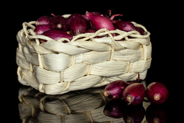 Lot of whole small red onion bulb in bast basket isolated on black glass