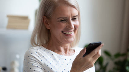 Fototapeta na wymiar Aged woman holding smartphone looks at screen read pleasant sms