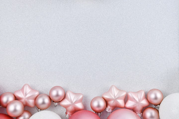 Seasonal Christmas background with white and pink tree baubles in shape of balls and stars at bottom and empty copy space with silver white glitter background at top