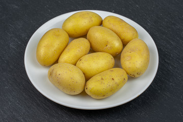 Lot of whole pale yellow potato on white ceramic plate on grey stone