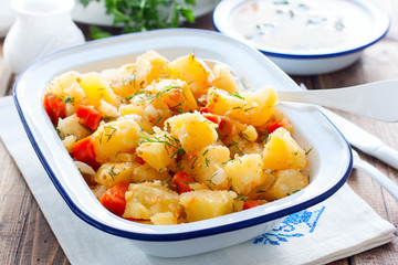Baked sliced potatoes with carrots and onions in an enameled form, horizontal