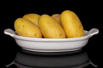 Group of five whole pale yellow potato in white oval ceramic bowl isolated on black glass