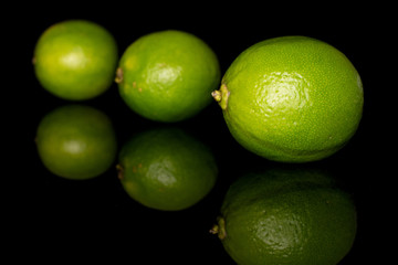 Group of three whole sour green lime diagonal isolated on black glass