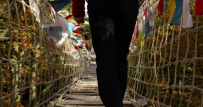 Older women with backpack passing Himalayan sidewalk path Skywalk wooden construction with colored flags during windy, sunny autumn day captured in Radhost Pustevny area slow motion 4k 60fps