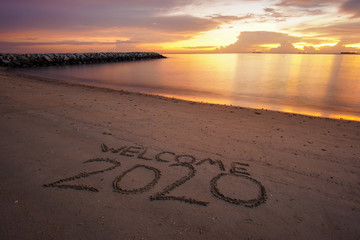Welcome 2020 written on the sandy beach during sunset.