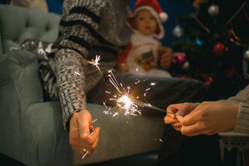 Father, mother and son holding sparklers at home. Dad lights a sparkler. Happy family concept.