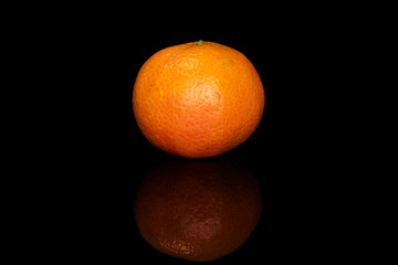 One whole fresh orange mandarin isolated on black glass