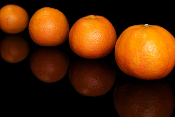 Group of four whole fresh orange mandarin diagonal isolated on black glass