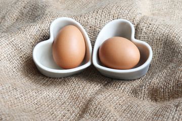 Chicken Eggs are placed in a heart shaped white ceramic container concept On a brown sack  close up isolated space for background texture