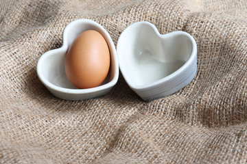 Chicken Eggs are placed in a heart shaped white ceramic container concept On a brown sack  close up isolated space for background texture