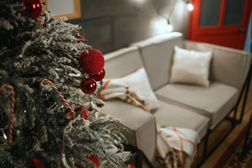 Christmas tree and sofa in living room decorated for New Year and Christmas. Focus on red christmas balls.