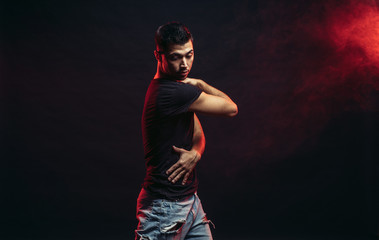 Young man professional dancer fond of dancing. dancing movements by caucasian man isolated in studio with red smoky background