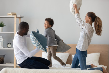 Overjoyed mixed race family of three fighting with pillows.