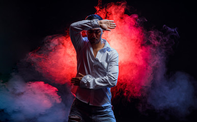 Obraz premium portrait of skillful caucasian man wearing white shirt move hands and arms during dance isolated over colorful smoky background