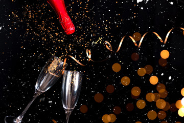Two champagne glasses and bottle with golden sparkles over black background. Happy new year.