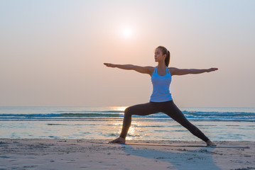 Fototapeta na wymiar Yoga woman doing yoga warrior pose on the beach for wellbeing health lifestyle.