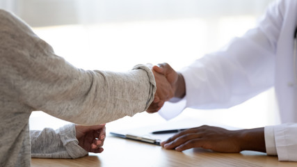 Close up african american doctor shaking hands with young woman.