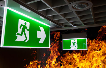 Hot flame fire and green fire escape sign hang on the ceiling in the office at night. The concept...