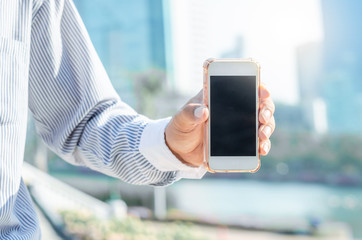 close up business man using hand hold smartphones with blank screen outdoor in city with sunrise and building background. 5G technology connecting the world.