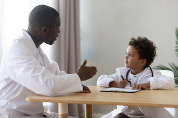 Happy little patient in doctors uniform plating with pediatrician.