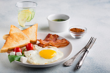 English breakfast concept. Fried eggs, bacon slices, spices, cherry tomatoes and slices of toast on a white background
