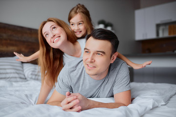 Fototapeta premium wspaniali kaukaski rodzice leżący na łóżku ze swoją córeczką, ubrani w zwykłe ubrania, szczęśliwa uśmiechnięta rodzina razem w domu