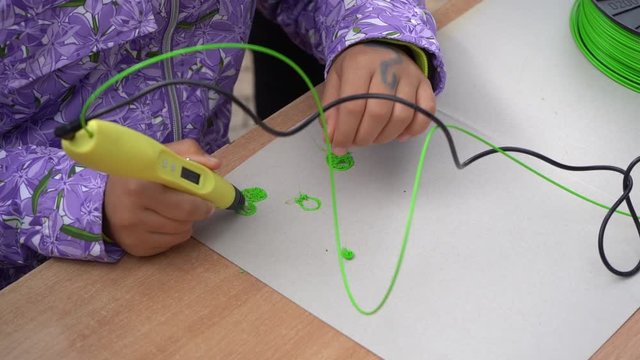 Closeup view of little girl hands using yellow modern 3d printing pen. Real time full hd video footage.