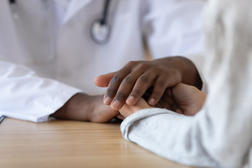 Young woman holding hands of african american male doctor, closeup. - Powered by Adobe
