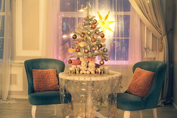 A beautiful room decorated for Christmas: a table with an openwork tablecloth, a small New Year tree with garlands, two velvet chairs with pillows and a luminous star on the window.