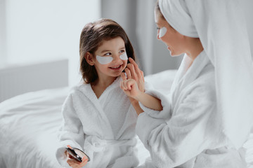 beautiful mother in bathrobe and her little daughter together with towels on head and mask on face...