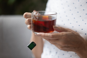 Closeup view elderly female hands holding cup with black tea