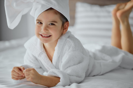 beautiful cute little girl of caucasian appearance wearing bathrobe and towel, lies on bed