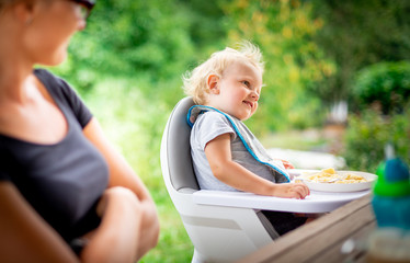 Baby sitting in high chair eating with his mom outdoor