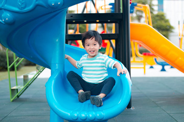 Young asian boy playing on a blue playground slide