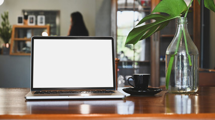 Laptop computer mockup empty screen on wood table in coffee cafe.