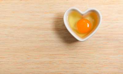 Chicken RAW freshness Yolk Eggs are placed in a heart shaped white ceramic container concept On wood close up isolated space for background texture