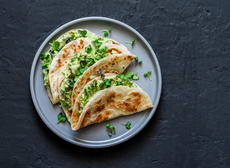 Avocado eggs greens salad paratha flatbread quesadilla on a dark background, top view