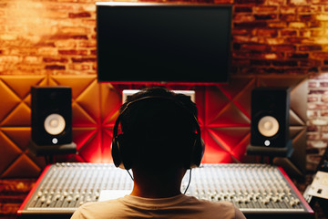 back of asian male music producer working on audio mixing console in recording studio. music...