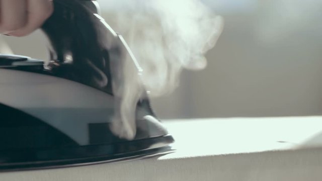 G irl's hands are ironing clothes on ironing board with a black iron close-up. Iron with steam and water stream.