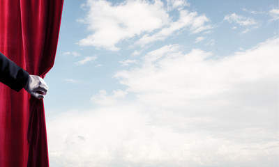Cloudy landscape behind red curtain and hand holding it