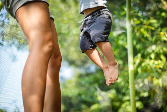 Legs Of Mom And Her Child While Jumping On Trampoline At Backyard