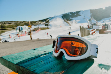 detail of some snowboard goggles on a green table in a ski resort full of snow and people
