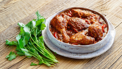 chicken chakhokbili with vegetables, herbs, and spices in a fleck ceramic plate on wooden background