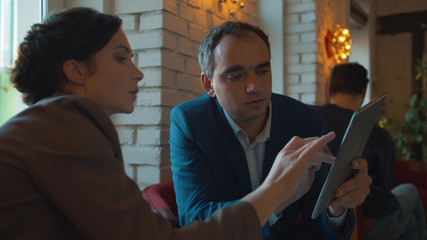 Man and woman at meeting look on a tablet and discuss