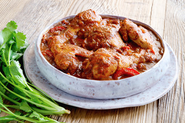 hot chicken stew with vegetables, herbs, and spices in a fleck ceramic plate on wooden background